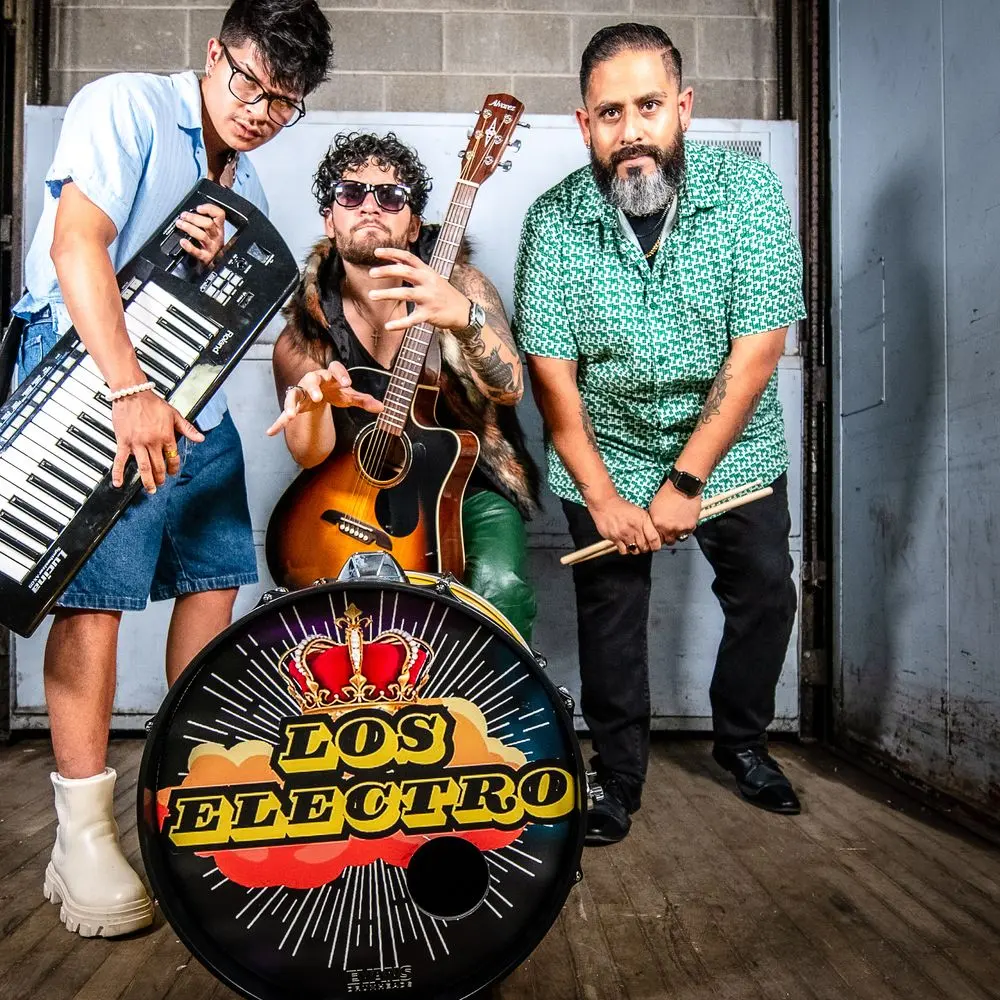 The three members of Los Electro posing with instruments and their named bass drum in the band’s official press-kit photo.
