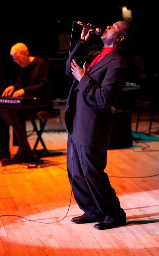 Ty Causey singing into a microphone on stage, with a keyboard player behind him.